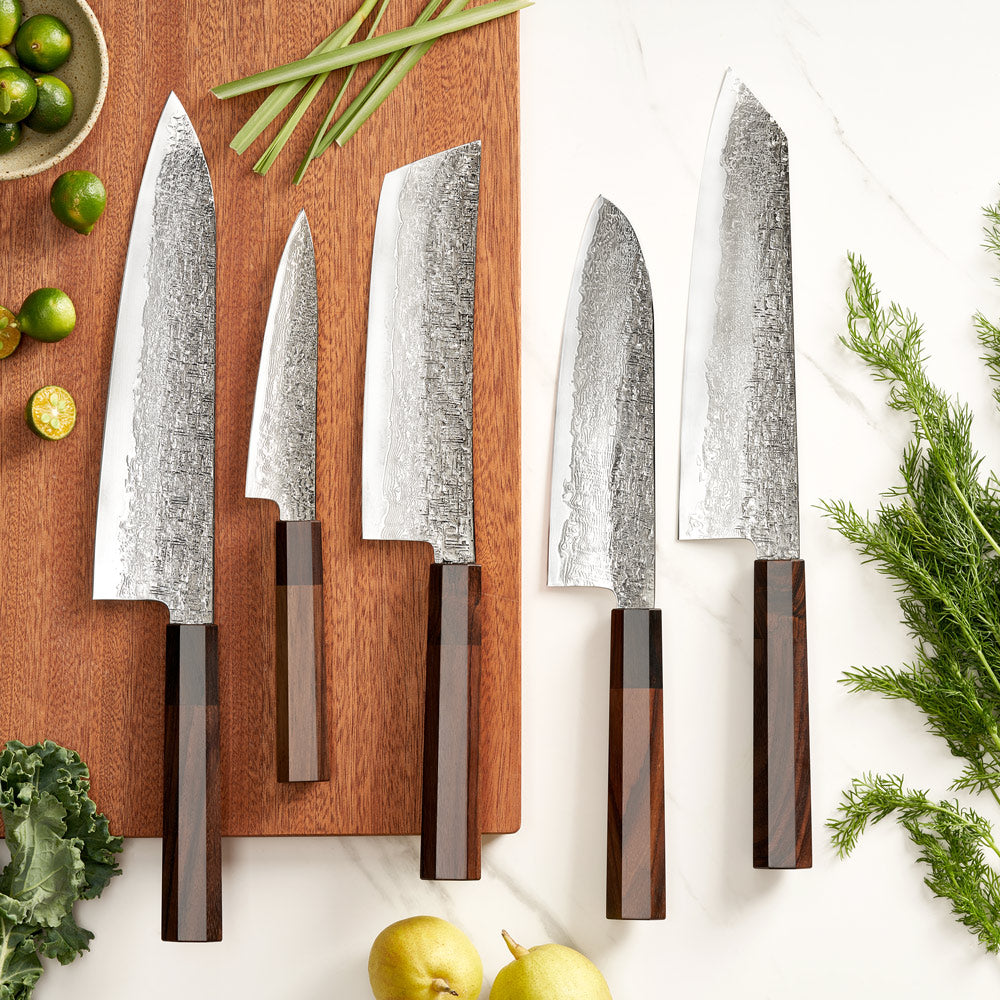 Set of five knives with wooden handles on a wooden cutting board with fresh vegetables.