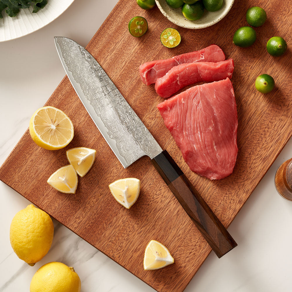 Wooden cutting board with raw meat, a knife, and citrus fruits on a light surface.