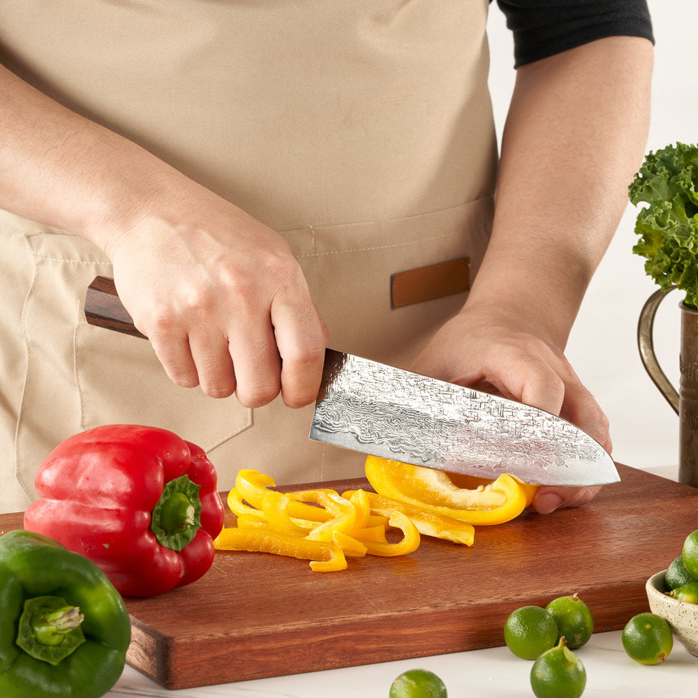 Person slicing bell peppers on a wooden cutting board with a chef's knife.