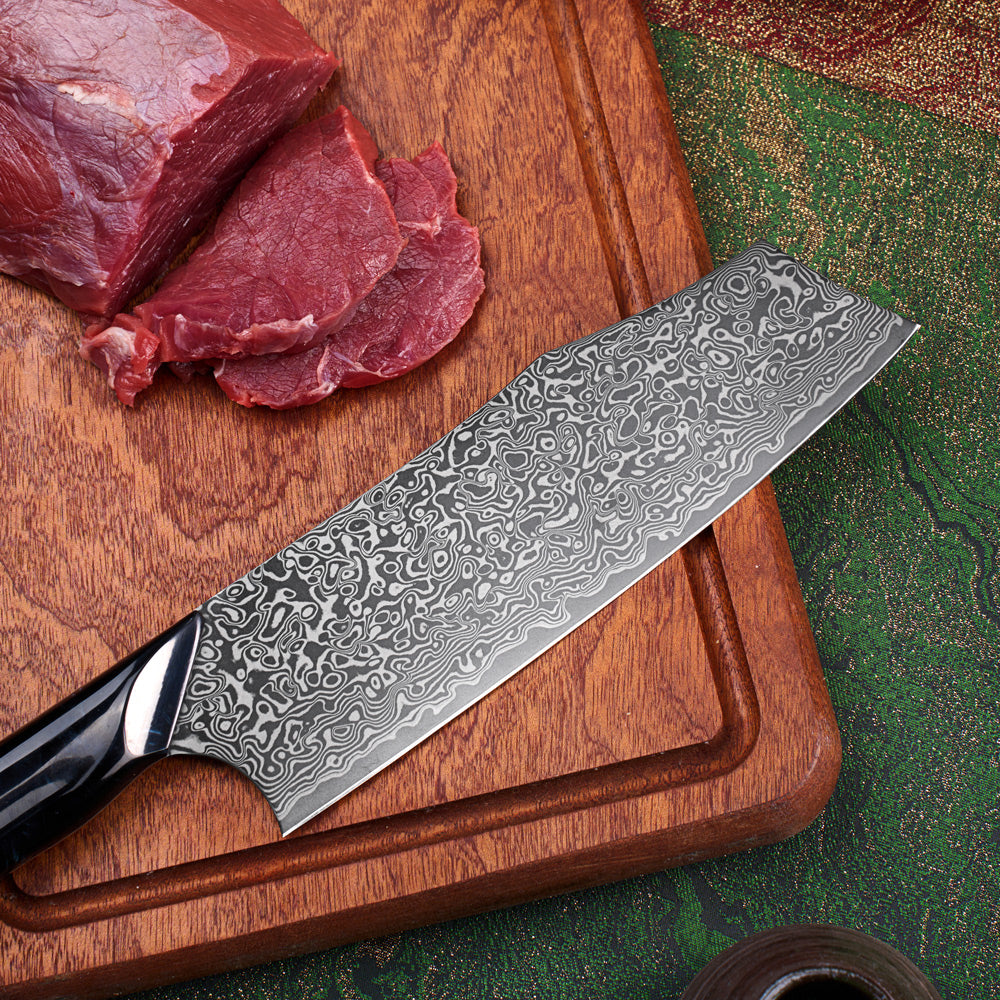A Damascus steel kitchen knife with a black handle rests diagonally on a wooden cutting board next to raw red beef slices.