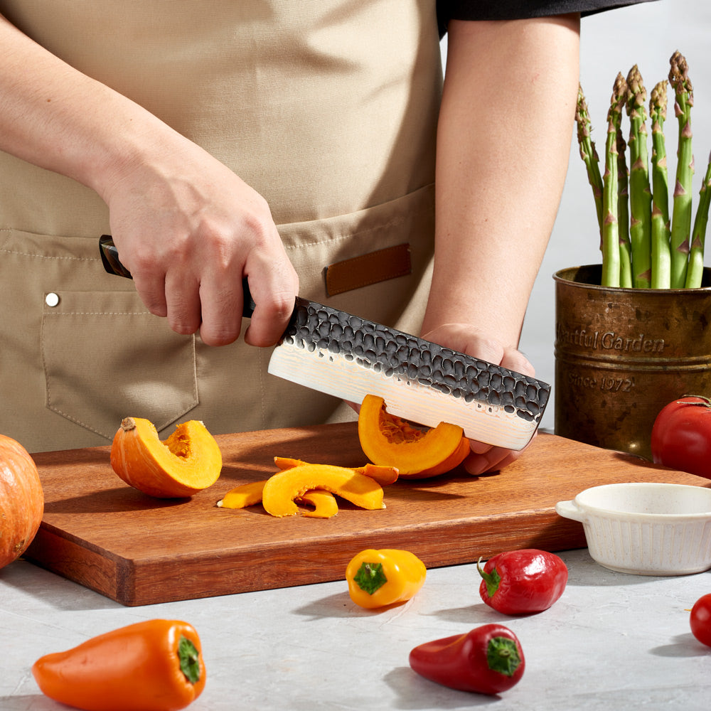 Person using a premium knife for Vegetables to cut pumpkins on a wooden cutting board with vegetables around.